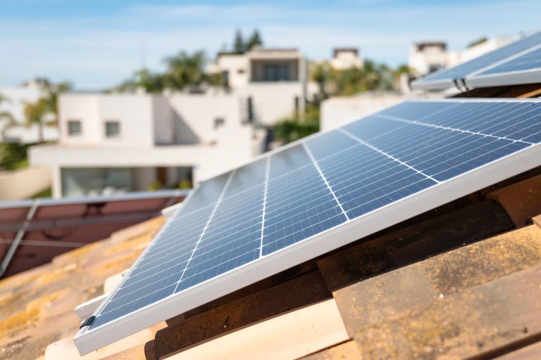 Imagen de placa solar sobre el techo de un unifamiliar, al fondo urbanización difuminada, utilizada en la sección "Proyectos desacados en energía solar" de la página home